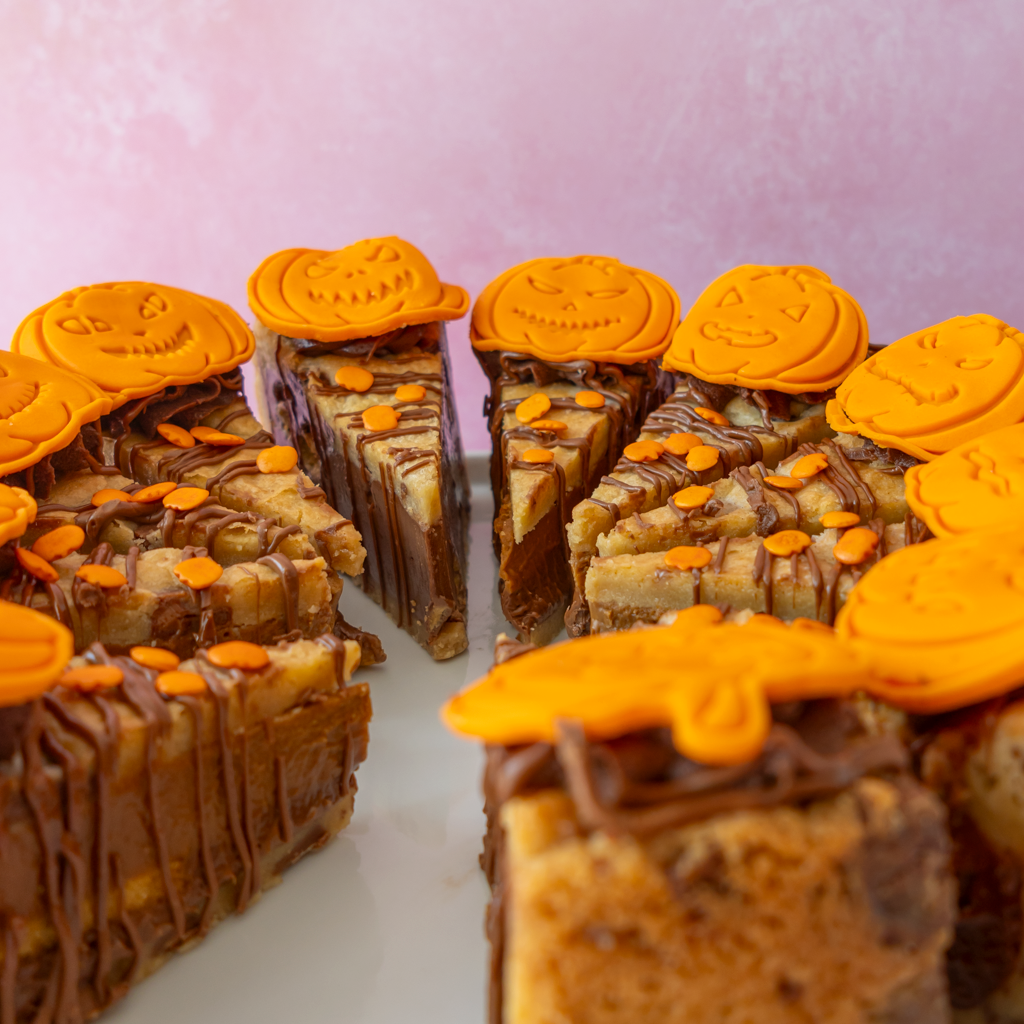 Halloween-themed chocolate cookie pie topped with orange pumpkin-shaped decorations, shown on a white plate against a soft pink background.