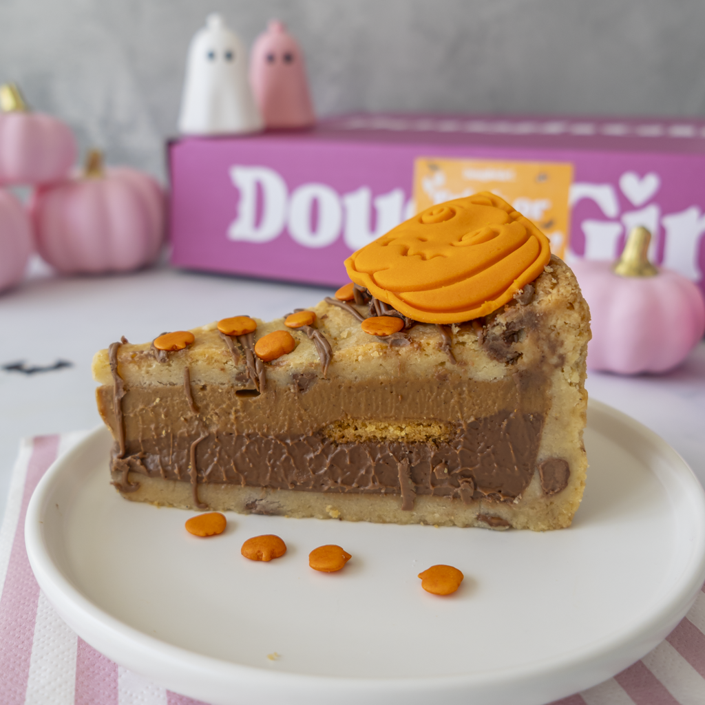 A slice of the full Pumpkin Patch Cookie Pie with a thick chocolate custard filling, topped with an orange pumpkin decoration and orange candy pieces, served on a white plate with a pink striped napkin.