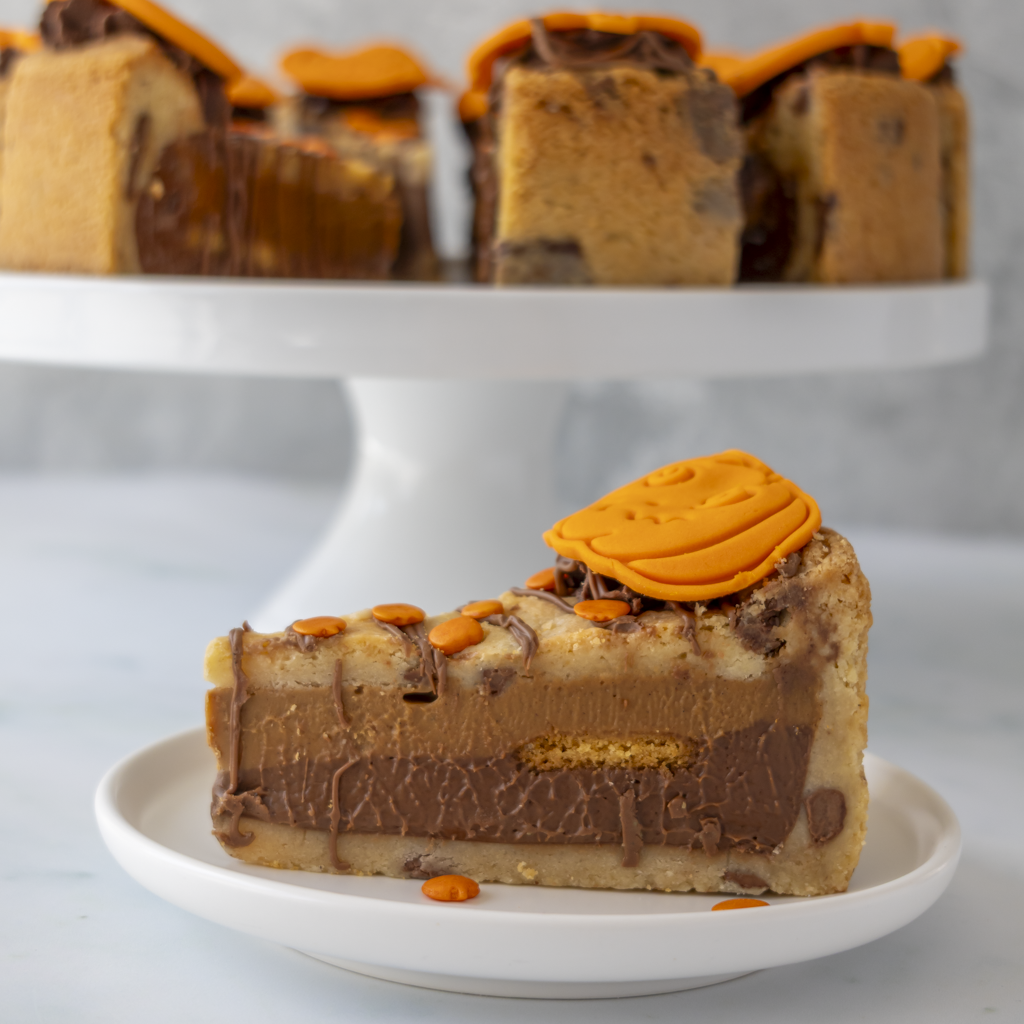 A slice of layered chocolate cookie pie with cookie crumb sides and a piped orange frosting swirl, served on a small white plate with more slices on a cake stand in the background.