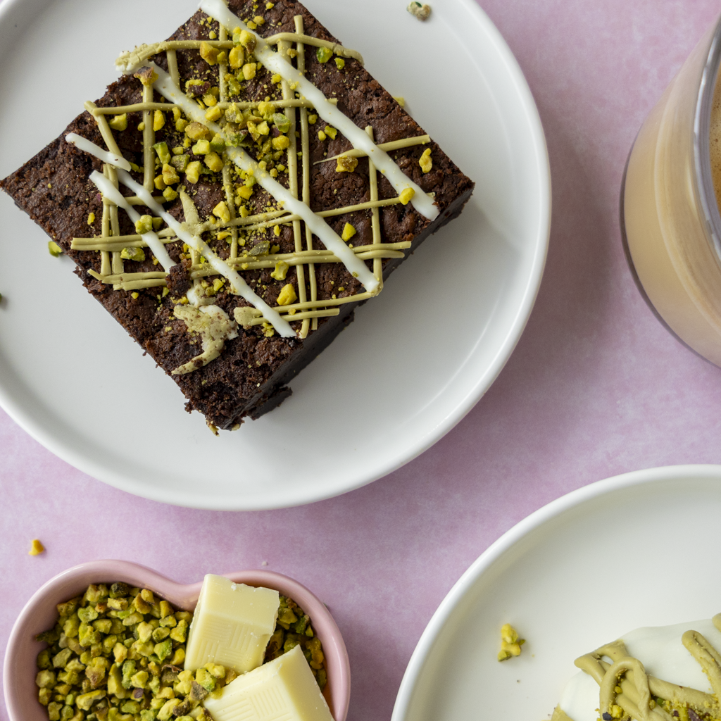 Pistachio Brownie Slab served on white plate with crushed pistachios and creamy topping