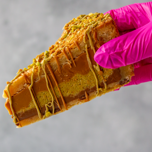 Pistachio Kunafa and Biscoff Cookie Pie held by a hand wearing a pink glove against a gray background