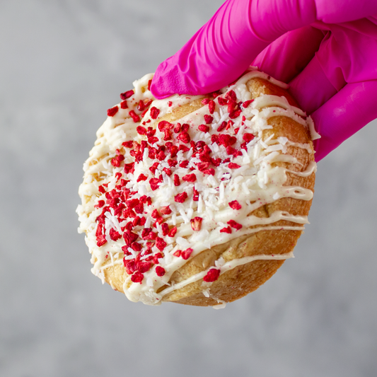 Raspberry, Coconut & White Chocolate Stuffed Deluxe Cookie held by a gloved hand against a gray background