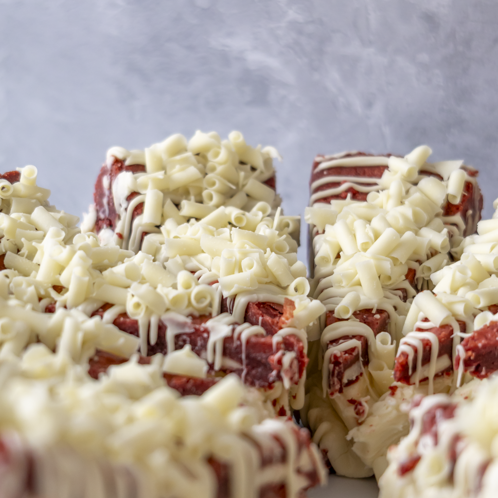 Red velvet cookie pie slices topped with shredded white chocolate and drizzled white chocolate, arranged on a white surface against a gray background.