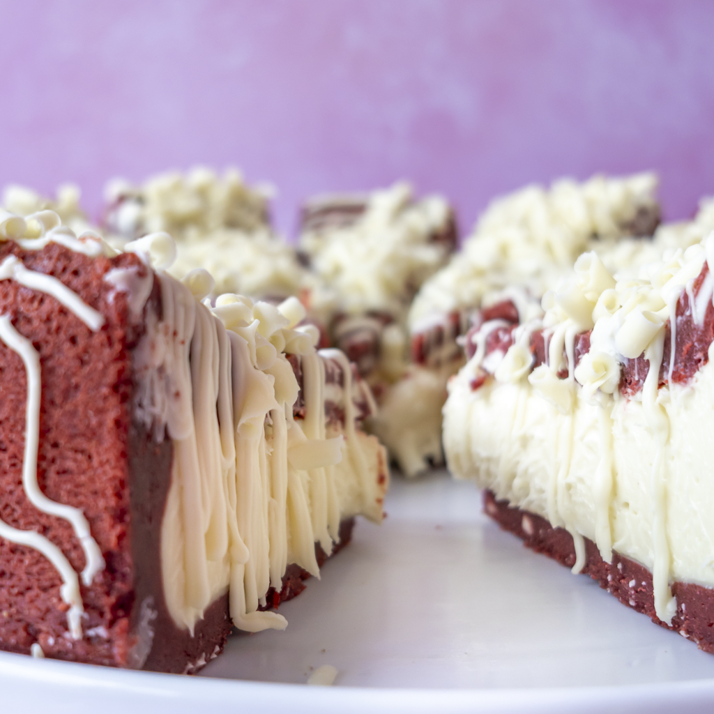 Red velvetcookie pie slices topped with white chocolate drizzle, served on a white plate against a soft pink background.