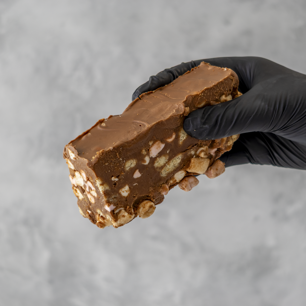 Hand holding a large piece of handmade Rocky Mountain Rocky Road Slab with nuts against a gray background