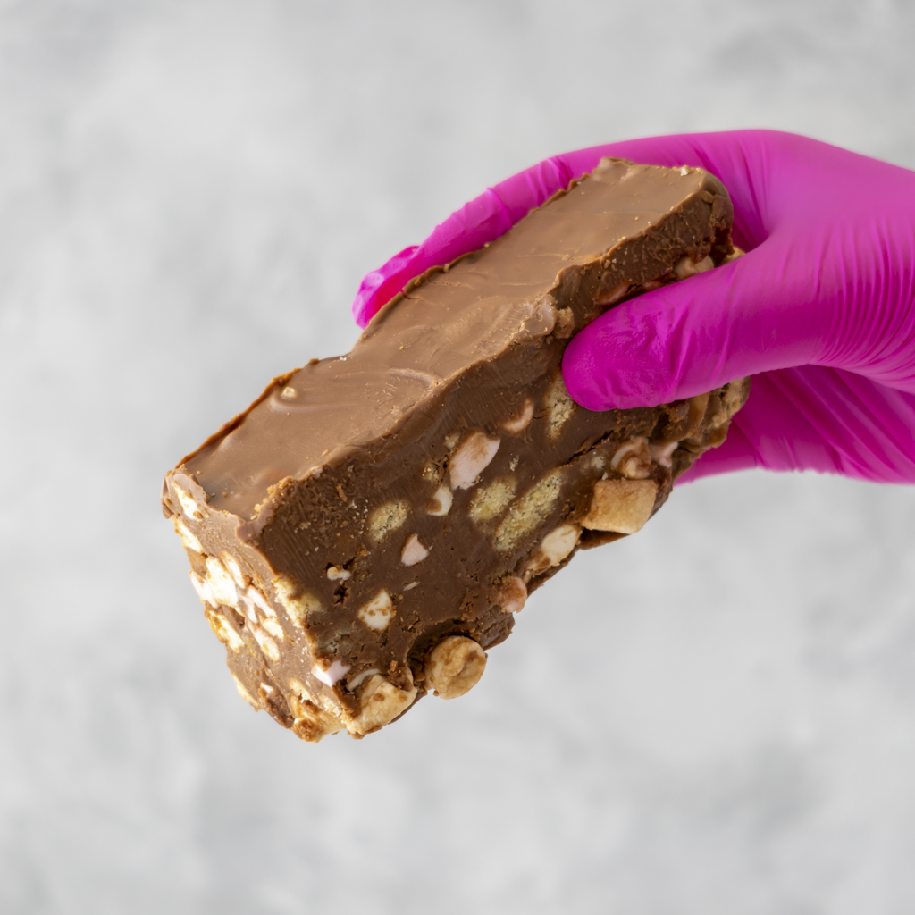 A Rocky Mountain Rocky Road Slab held by a hand wearing a pink glove on a light gray background
