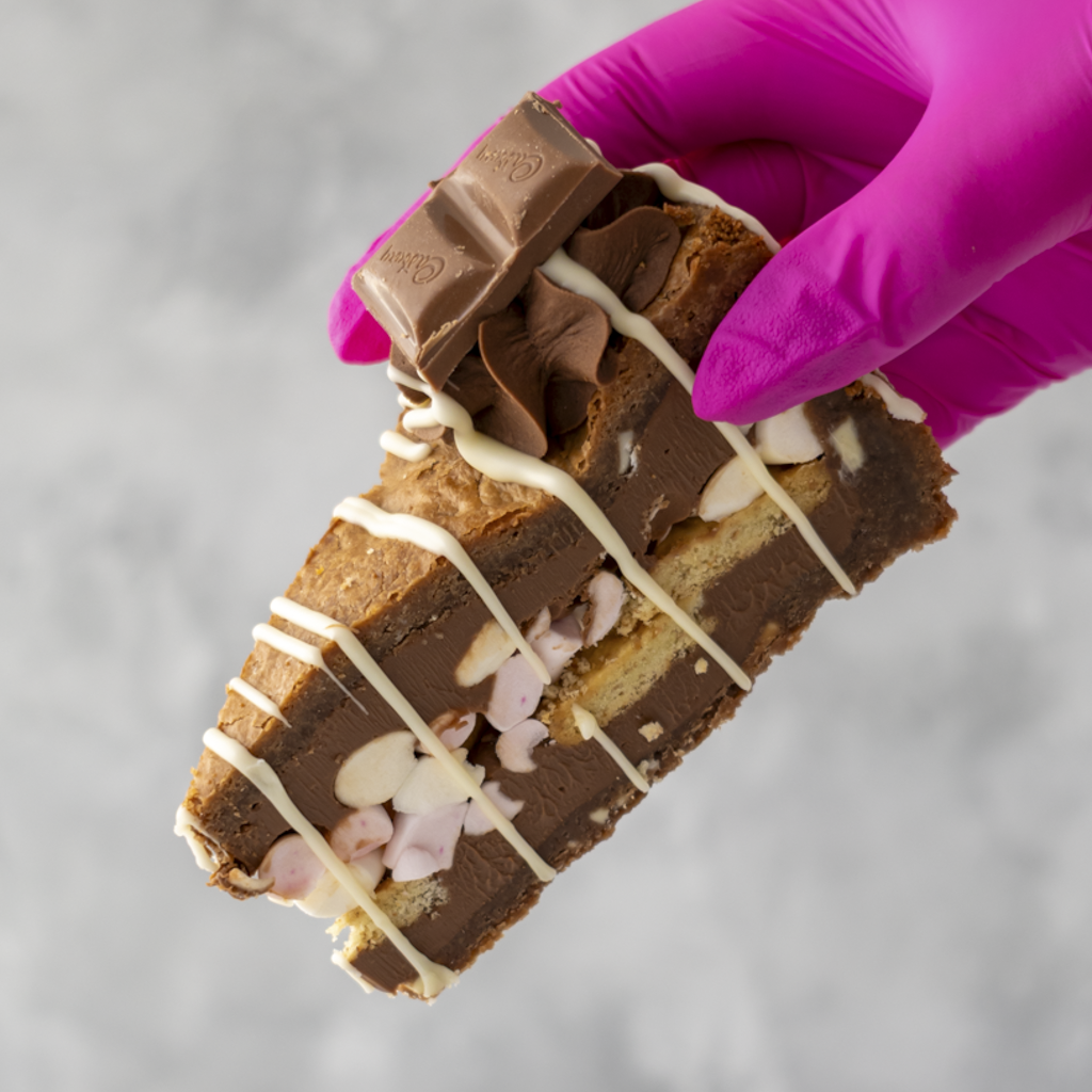 S'mores Cookie Pie Slice dessert bar with KitKat piece held by a gloved hand on a gray background