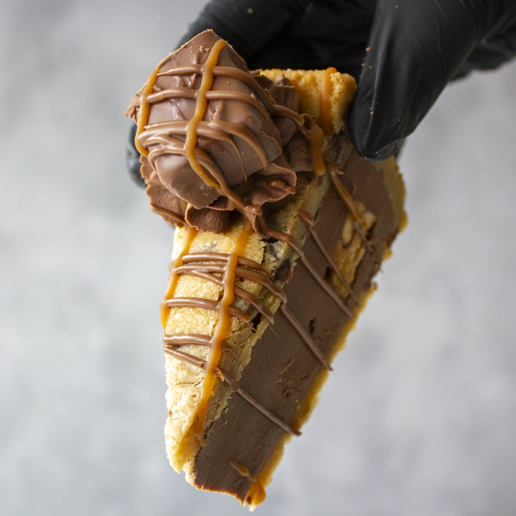Cookie Pie Slice with Snickers held in black glove showing thick chocolate cookie pie layers