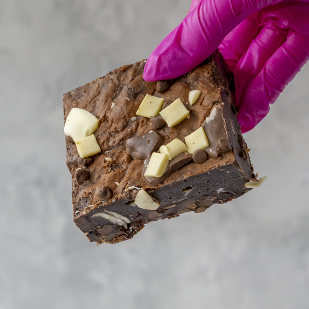 Triple Chocolate Brownie Slab held by a gloved hand on a gray background