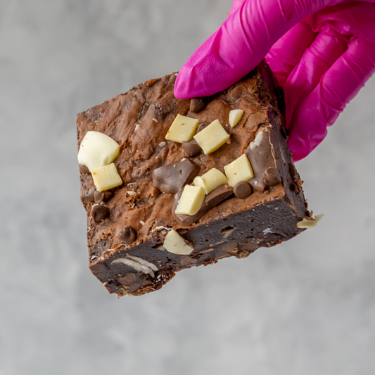 Triple Chocolate Brownie Slab held by a gloved hand on a gray background