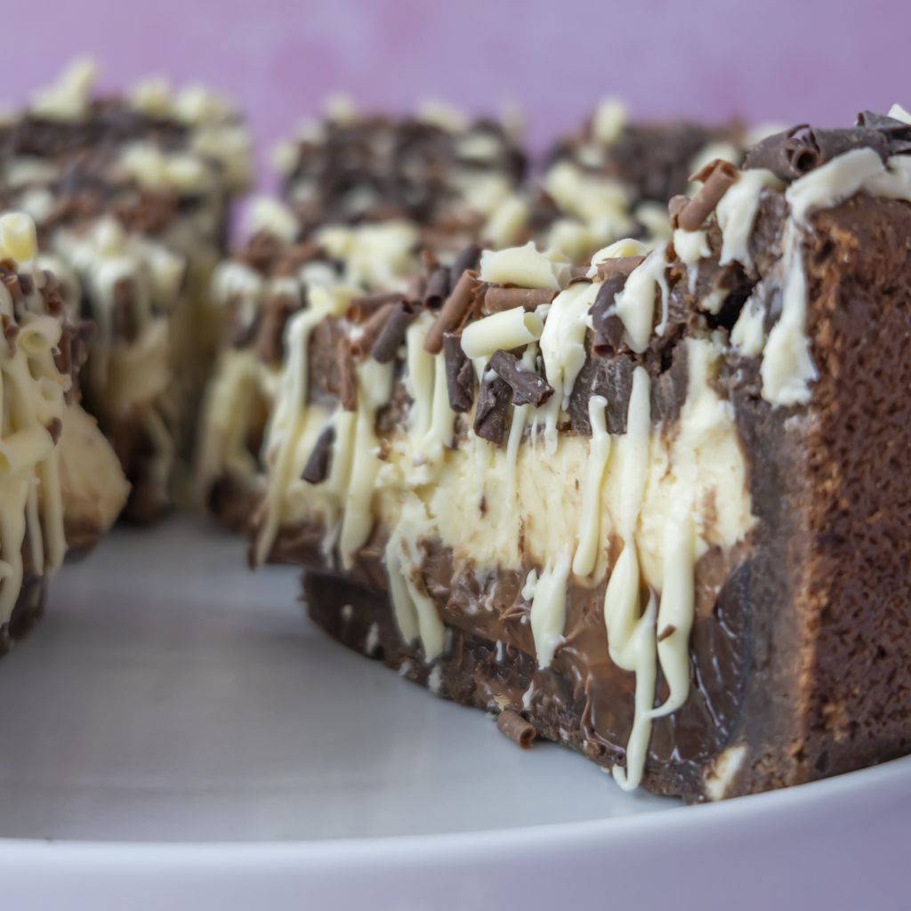 Chocolate chip cookie pie cut into slices, showing a thick layer of cream cheese filling, chocolate chips, and white chocolate drizzle on a white plate.