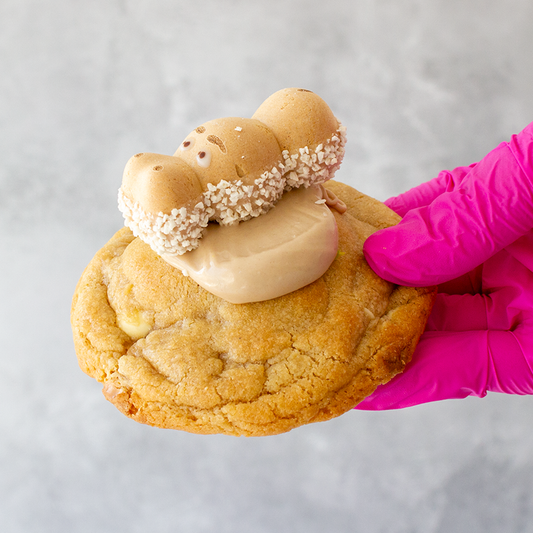 White Bueno Hippo Deluxe Cookie with cream filling held by a hand wearing a pink glove on a light gray background